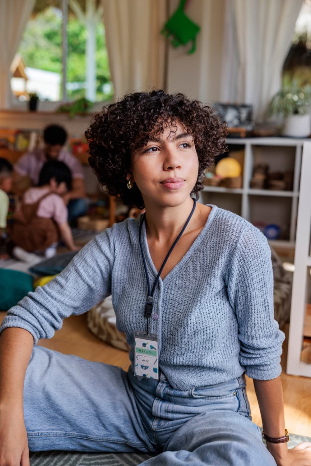 An educator with a lanyard in a classroom, children playing behind her